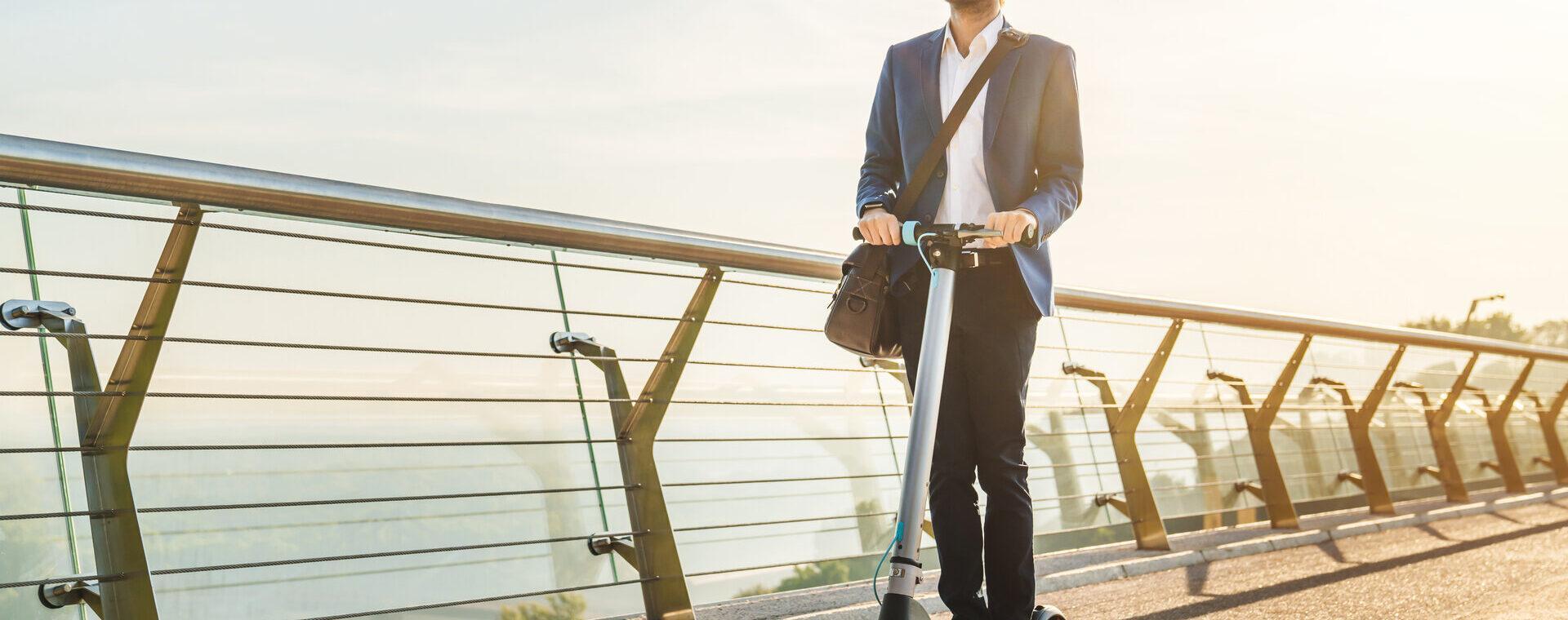 Junger Geschäftsmann im Anzug fährt E Scooter