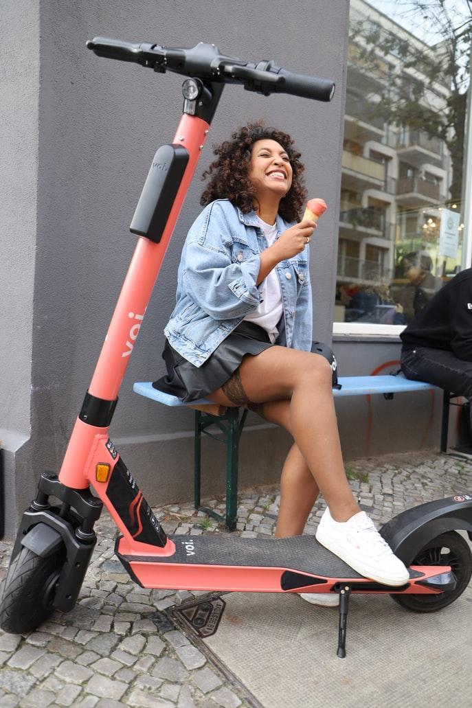Junge Frau an Straße mit E Scooter isst ein Eis