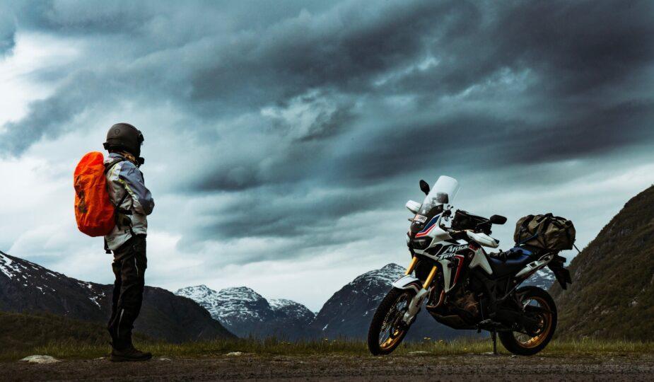 Mann mit Rucksack und Motorrad auf Reisen, stehen an einer Straße